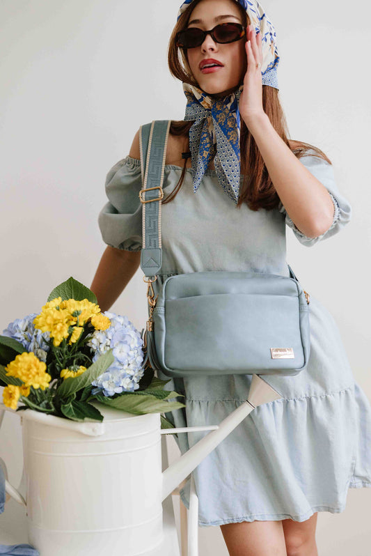 A red-haired woman modeling a Modern+Chic Dusty Blue Alice Crossbody Bag: Vegan Leather Bag, Key Leash & Wallet