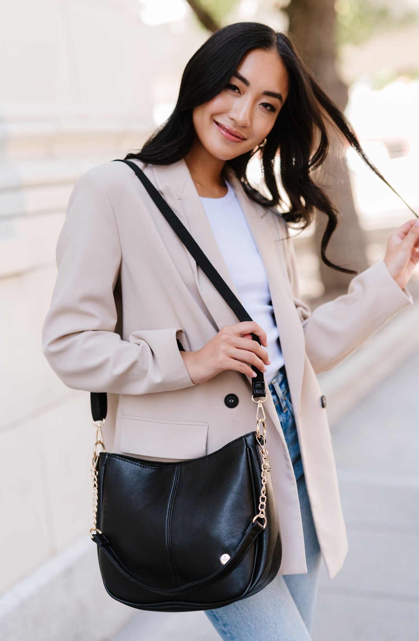 A woman standing in front of a white building wearing a black crossbody.