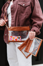 A woman wearing a crossbody clear bag and holding two additional clear bags.