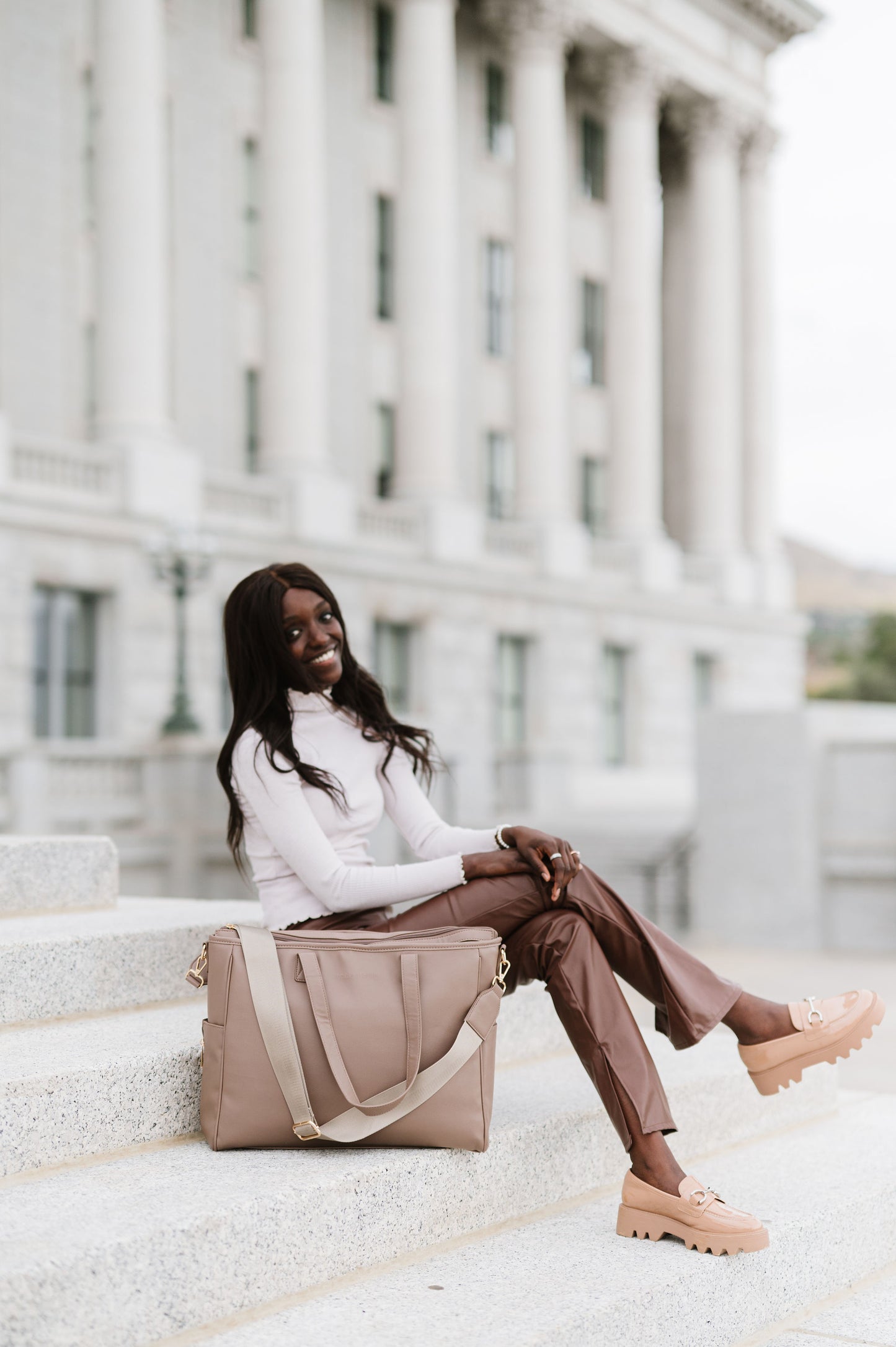 A woman sitting on cement steps with a taupe tote in front of her.