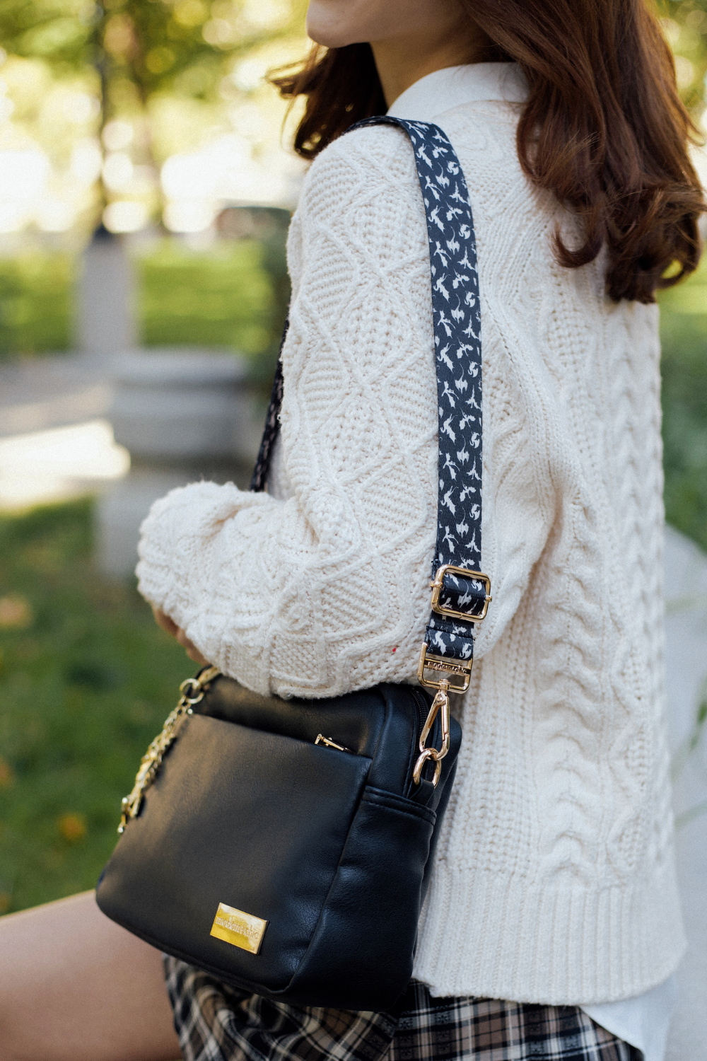 Person wearing a white cable-knit sweater, a black handbag, and a black-and-white dragon strap.