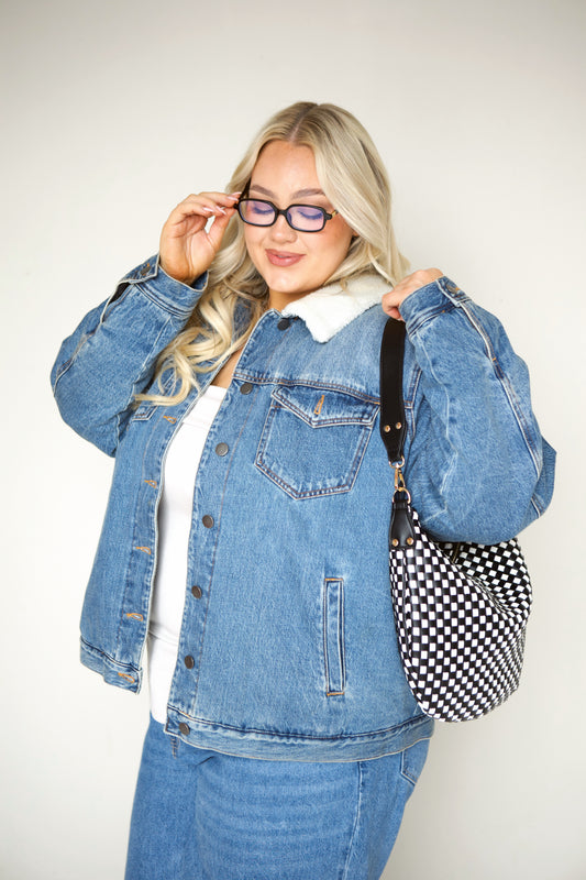 Woman wearing a denim jacket and jeans with a black vegan leather Modern+Chic Savannah Slouchy Tote on a white background.