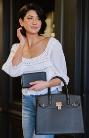 woman holding a black vegan leather tote bag on her arm and a matching black wallet in her hand