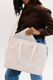 A woman pulling a laptop out of a cream tote.