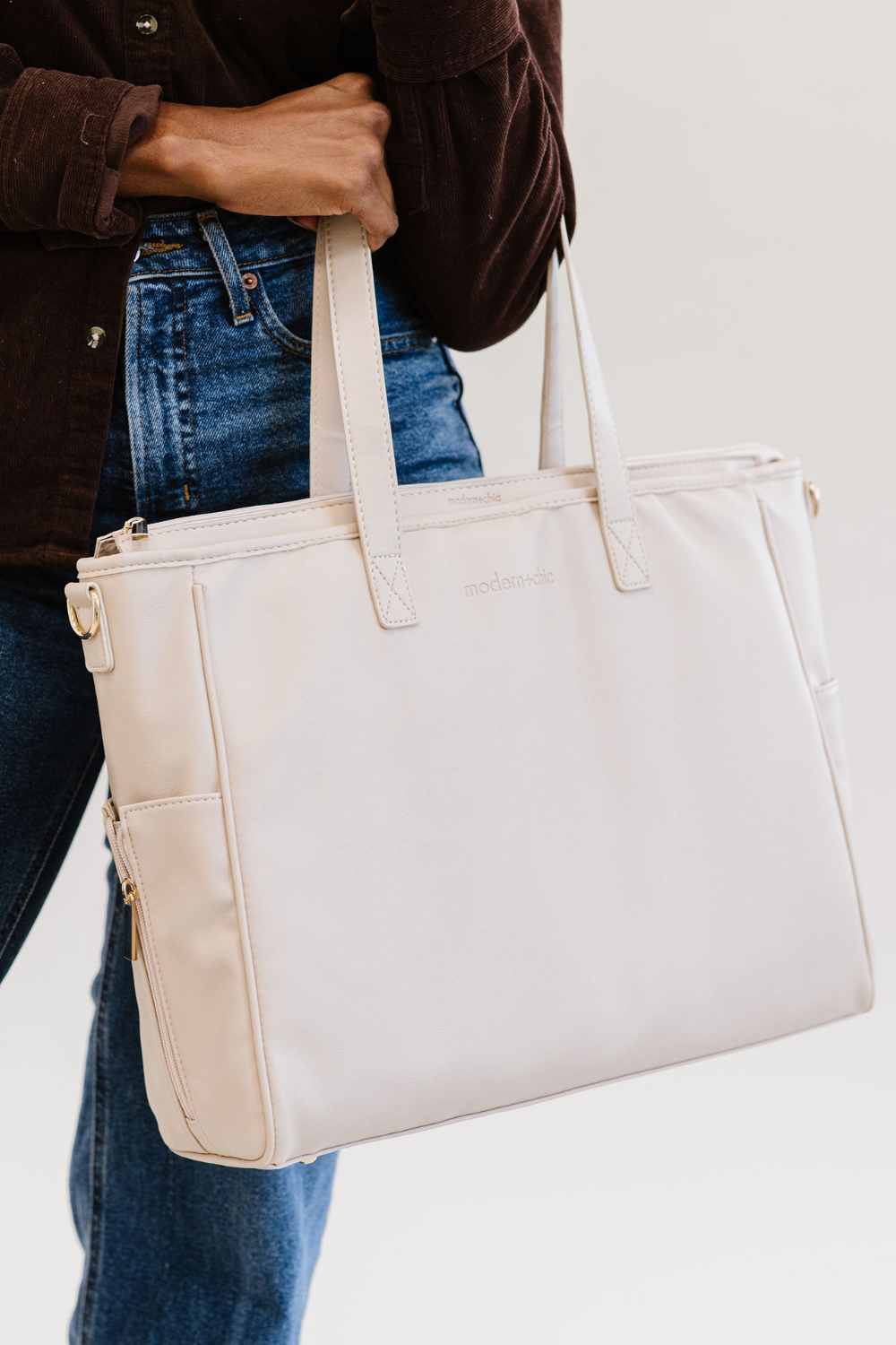 A woman holding a cream tote with the modern+chic logo on the front.