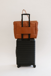 A brown tote with a luggage sleeve on a black suitcase.