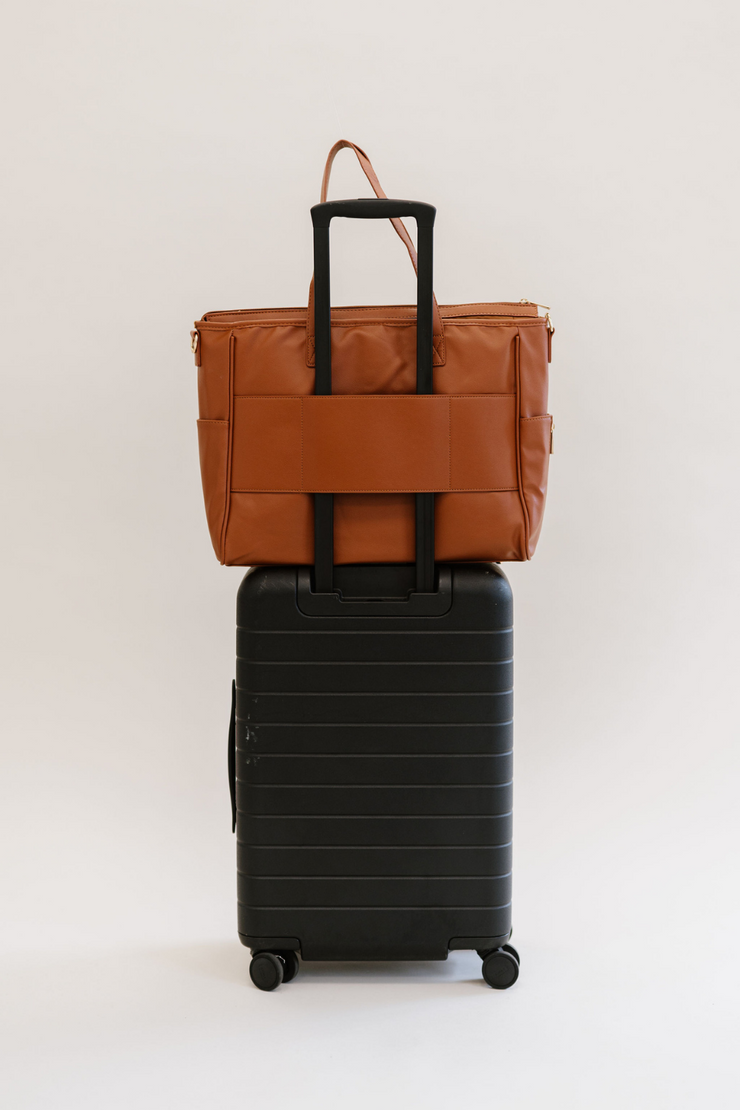 A brown tote with a luggage sleeve on a black suitcase.