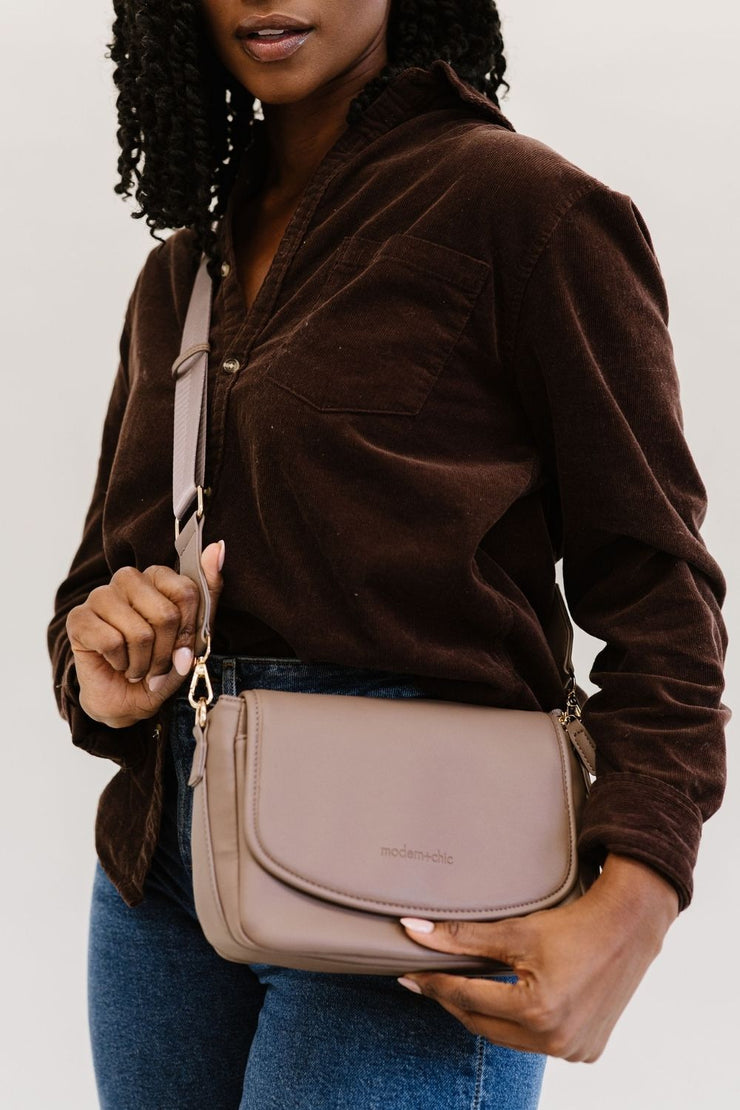 A woman wearing a taupe crossbody bag.
