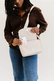 A woman putting her phone inside the front pocket of the cream crossbody.