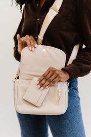 A woman wearing a cream crossbody and holding the matching cream wallet.