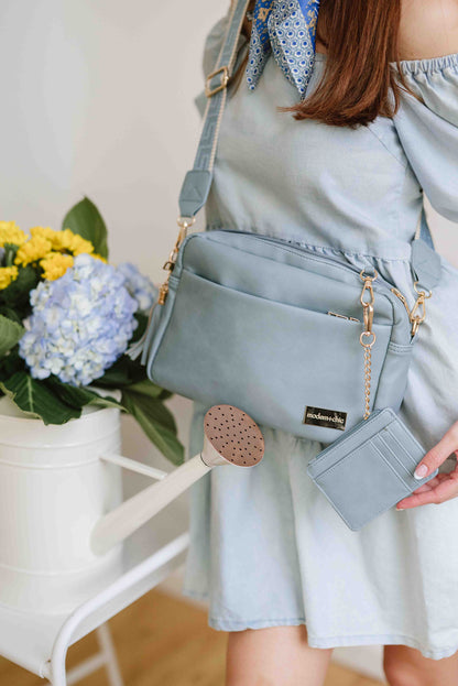 A red-haired woman modeling a Modern+Chic Dusty Blue Alice Crossbody Bag: Vegan Leather Bag, Key Leash & Wallet