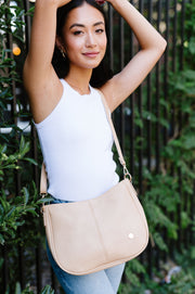 A woman standing in front of greenery and a fence wearing a cream crossbody.