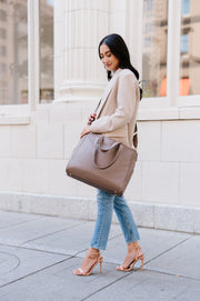 A woman wearing a taupe tote crossbody-style.