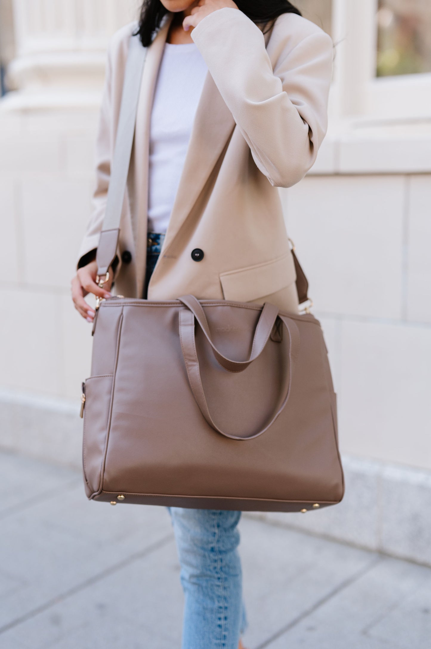 A woman wearing a taupe tote crossbody-style.
