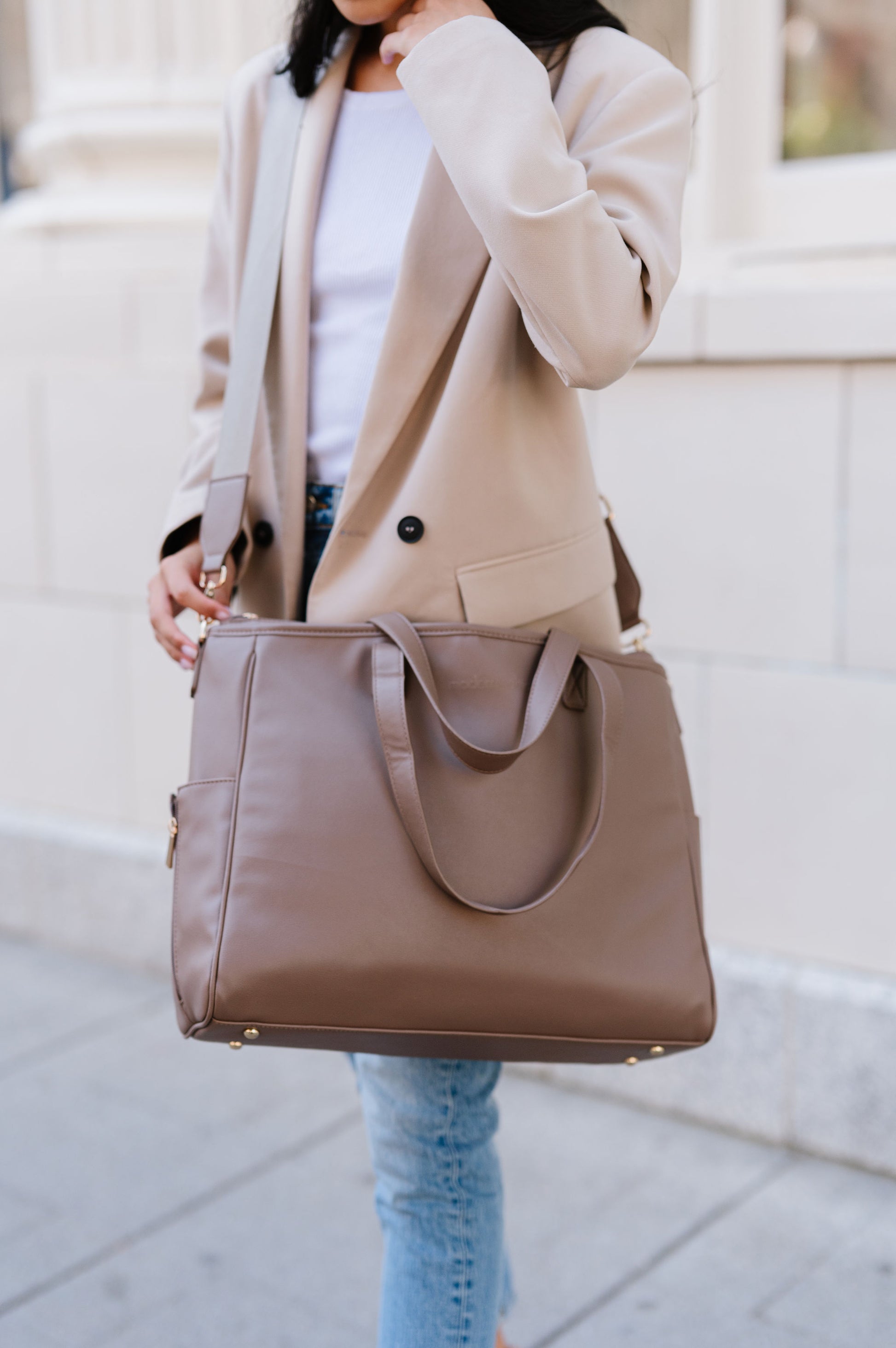 A woman wearing a taupe tote crossbody-style.