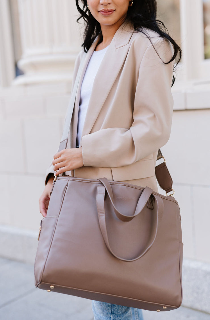A woman wearing a taupe tote crossbody style.