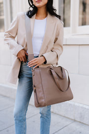 A woman wearing a taupe tote crossbody-style.