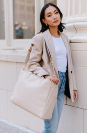 A woman wearing a cream tote on her shoulder.