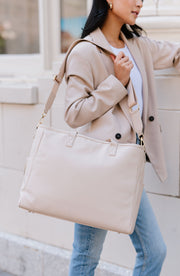 A woman holding a cream tote on her shoulder.