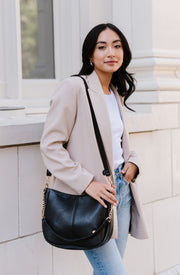 A woman standing in front of a white building wearing a black crossbody.