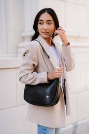A woman standing in front of a white building wearing a black crossbody.