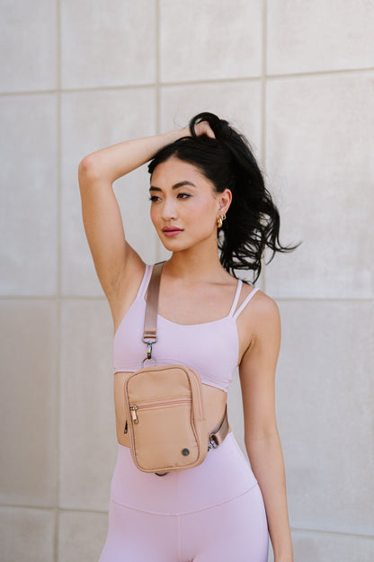A woman wearing a pink sports bra and leggings showing a Modern + Chic Lainey Convertible Crossbody Bag for Women on crossbody. 