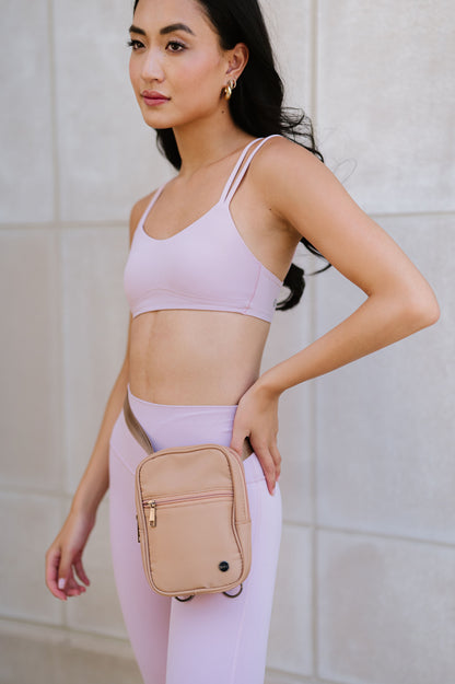A woman wearing a pink sports bra and leggings and a Modern + Chic Lainey Convertible Crossbody Bag for Women on around her waist.