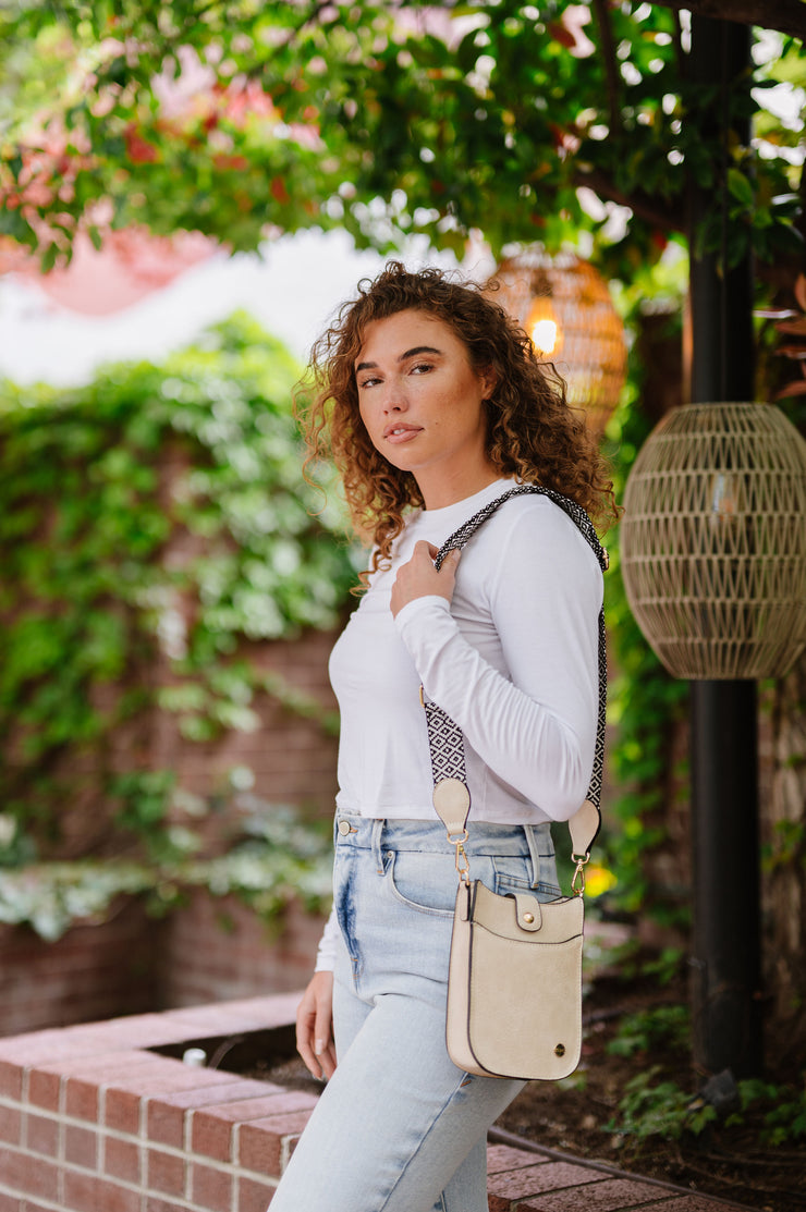 A woman wearing a ivory brown crossbody bag with a woven strap