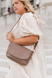 A woman wearing a cream crossbody bag.