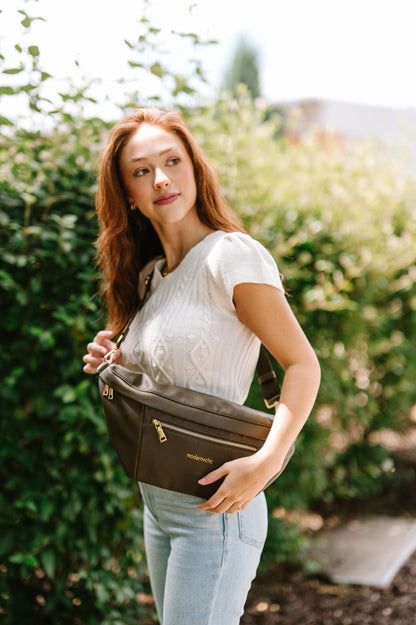A woman wearing a cropped white sweater vest and an oversized olive Modern+Chic Presley Oversized Sling Bag for Women with gold hardware over her hip.