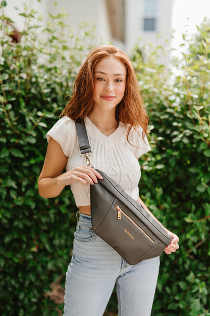 A woman wearing a cropped white sweater vest and an oversized olive Modern+Chic Presley Oversized Sling Bag for Women with gold hardware across her torso.