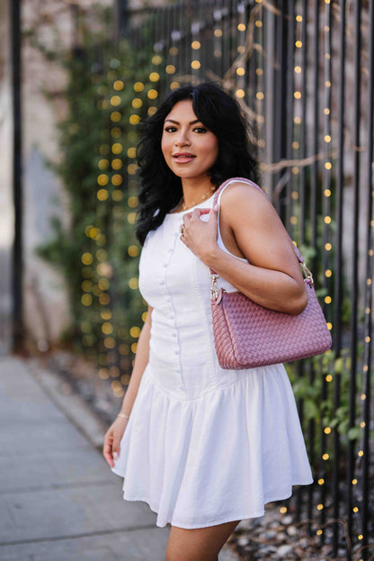 A woman wearing a pink Modern + Chic Elle Woven Crossbody Bag for Women over her shoulder outdoors.