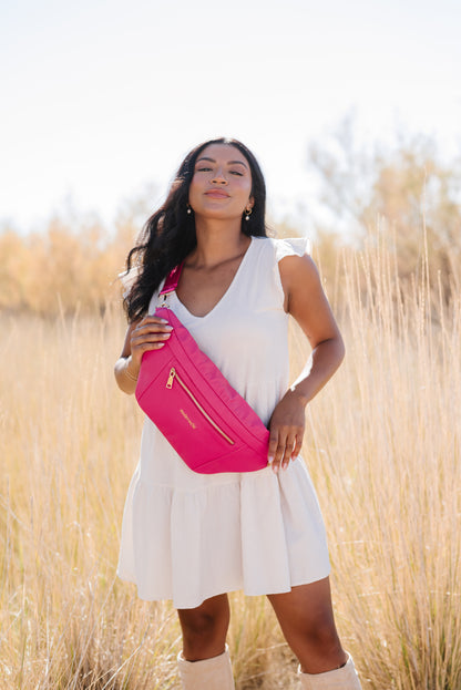A woman wearing a white dress and a hot pink oversized Modern+Chic Presley Oversized Sling Bag for Women with gold hardware across her torso.