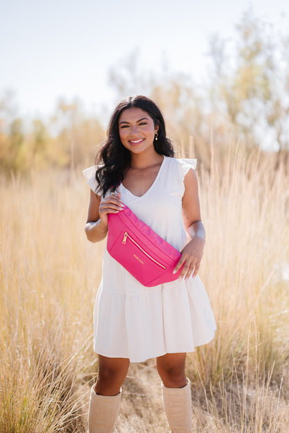 A woman wearing a white dress and tall boots with a hot pink oversized Modern+Chic Presley Oversized Sling Bag for Women with gold hardware across her torso.