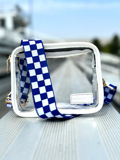 A clear handbag wrapped in a blue and white Modern + Chic Lizzie Checkered Purse Strap for Crossbody Bags sitting on an empty bleacher. 