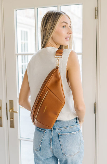A woman wearing a white sweater vest and an oversized camel Modern+Chic Presley Oversized Sling Bag for Women with gold hardware across her back.