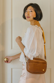 A woman opening a door and wearing a brown crossbody bag.