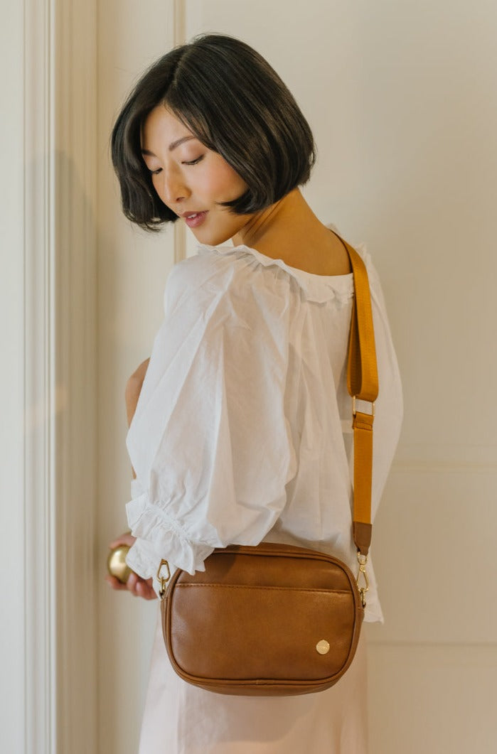 A woman looking over her shoulder and wearing a brown crossbody bag.