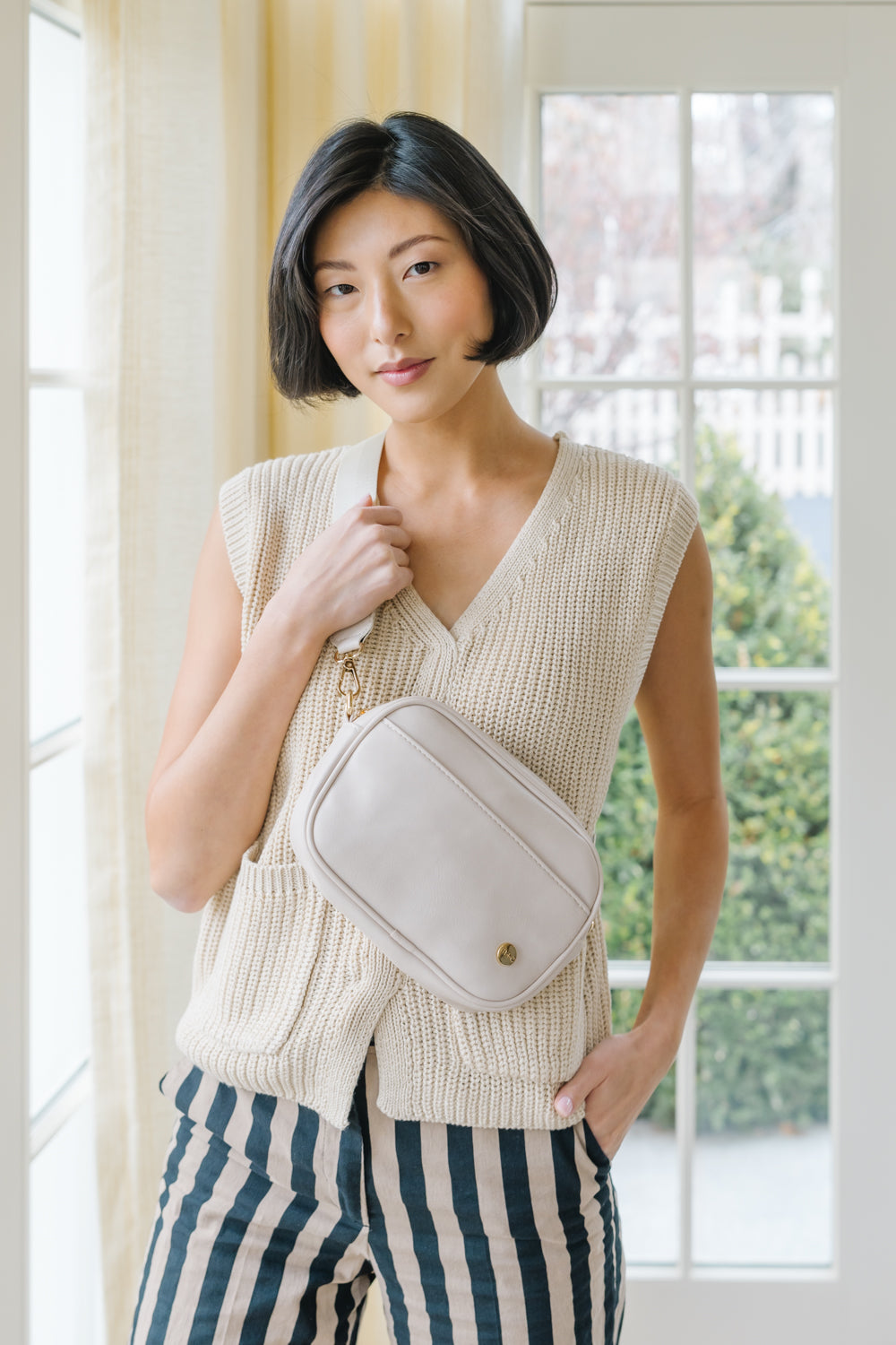 A woman wearing cream belt bag across her torso.