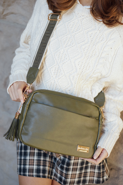 Person holding an olive green Modern + Chic Crossbody Vegan Leather Bag wearing a white sweater and plaid skirt.