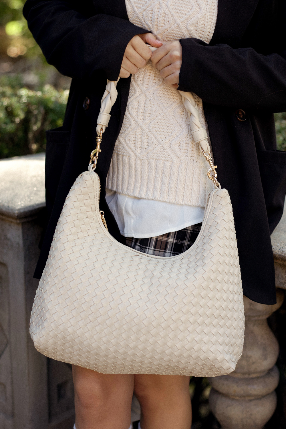 Person holding an ivory Modern+Chic Kelly Woven Convertible Crossbody Shoulder Bag outdoors.