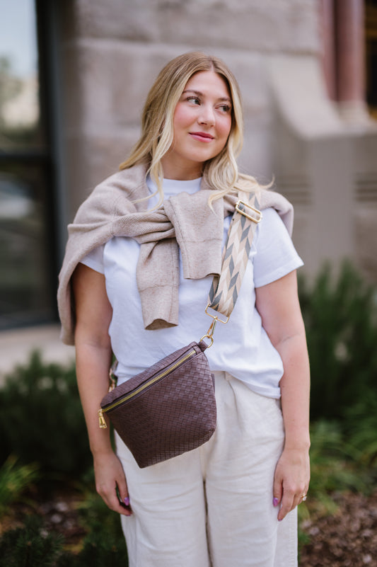 Woman wearing a white t-shirt, a sweatshirt tied around her shoulders and a brown criss cross style Modern + Chic Rory Oversized Belt Bag for Women with a gold zipper and hardware crossbody.