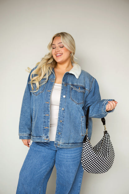 Woman wearing a denim jacket and jeans with a black and white woven vegan leather Modern+Chic Savannah Slouchy Tote on a white background. 