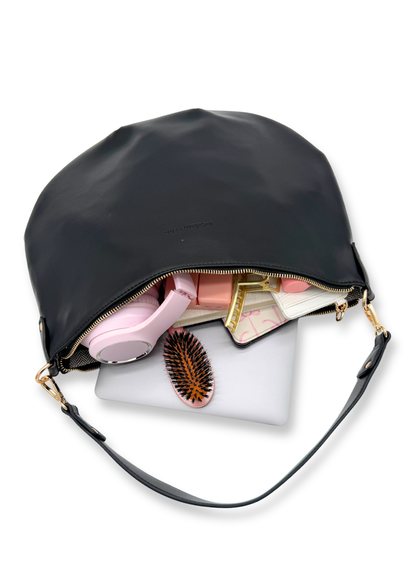 A black vegan leather Modern+Chic Savannah Slouchy Tote on a white background with a laptop, pink headphones, kindle and hairbrush on a white background. 