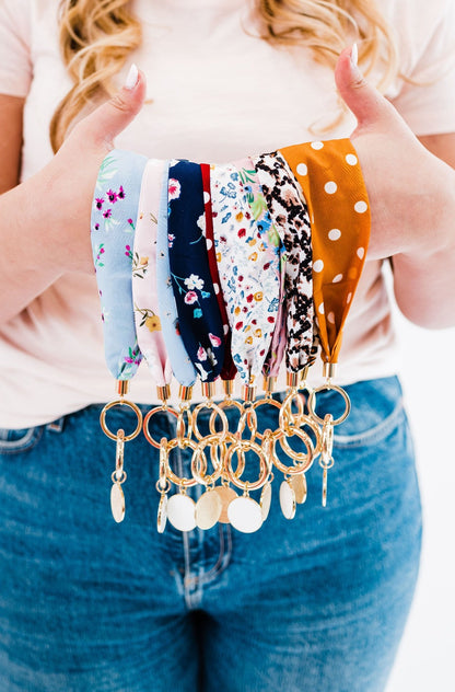 A person holding out Modern + Chic Luna Fabric Keychain Bracelets for Women-  showcasing various patterns and colors such as animal print, floral, dots, and plain colors.