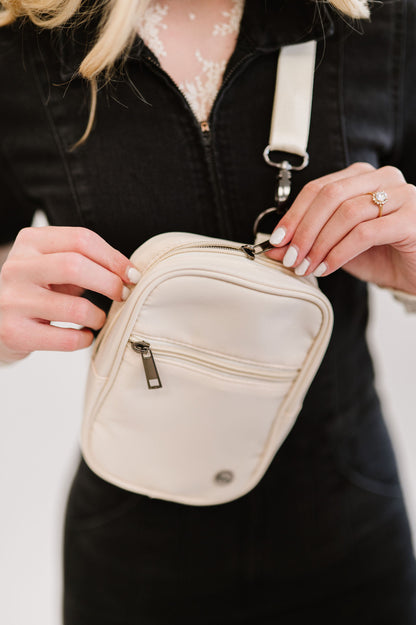 A closeup shot of a woman wearing a lace long sleeve top under a black jumpsuit and a white Modern + Chic Lainey Convertible Crossbody Bag for Women crossbody.