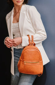 Woman holding a camel mini backpack on her arm with both straps hanging from her wrist. 