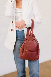 Woman holding a rose-colored mini backpack from her arm. 