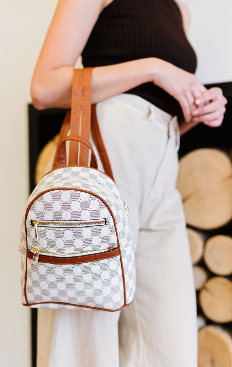 Woman holding small dome backpack on her arm. The backpack has a black and white circle pattern with contrasting camel trim. 