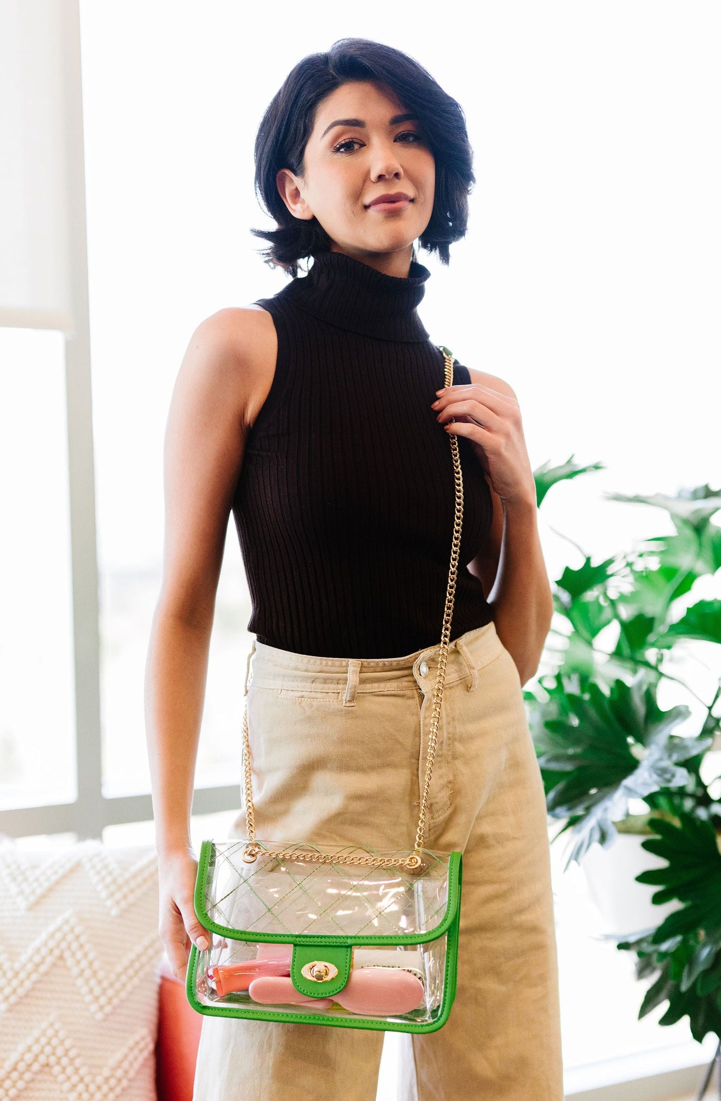 woman wearing green clear purse with gold chain strap, vegan leather trim